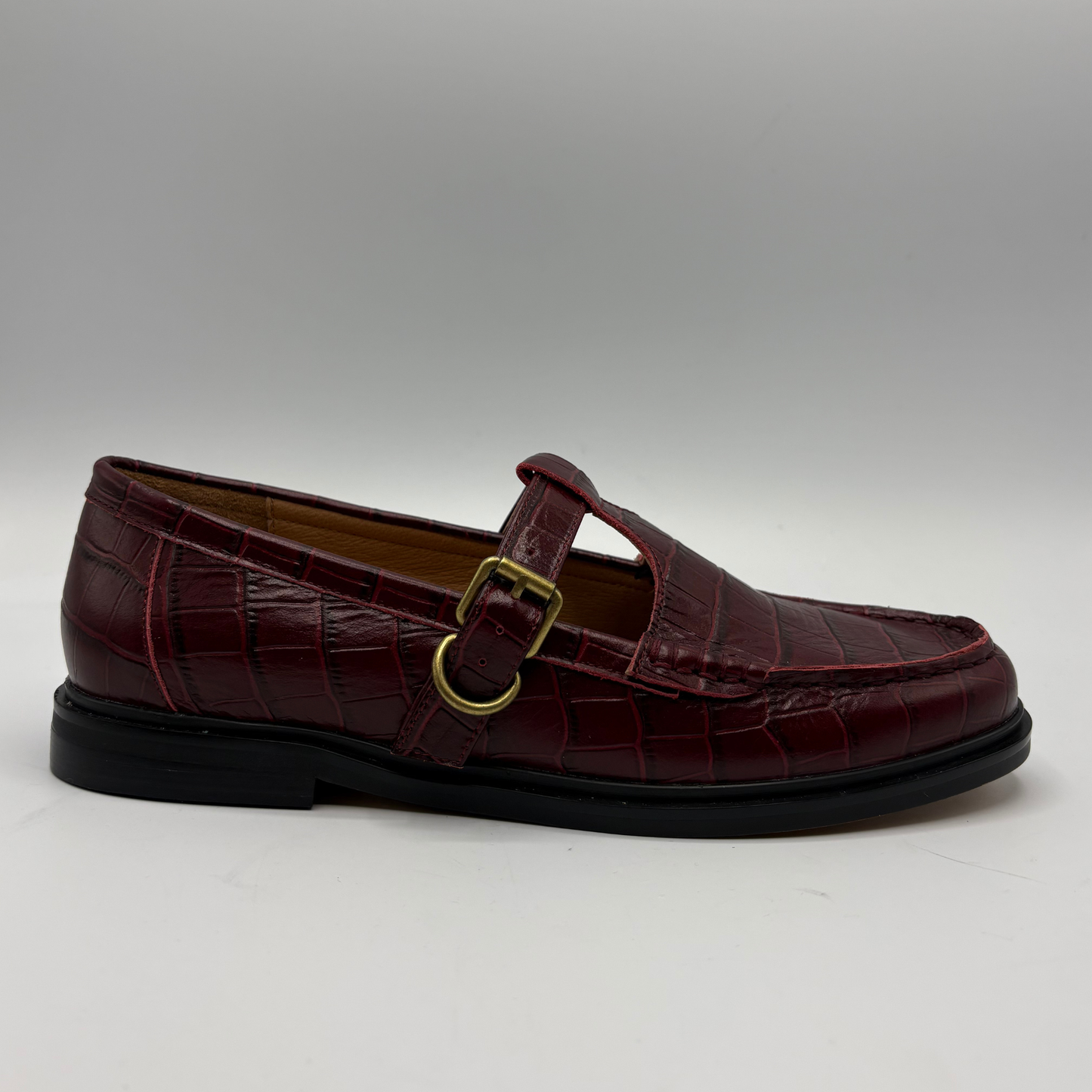 A single burgundy crocodile-embossed Mary Jane loafer with a gold buckle strap, shown in profile against a neutral gray background.