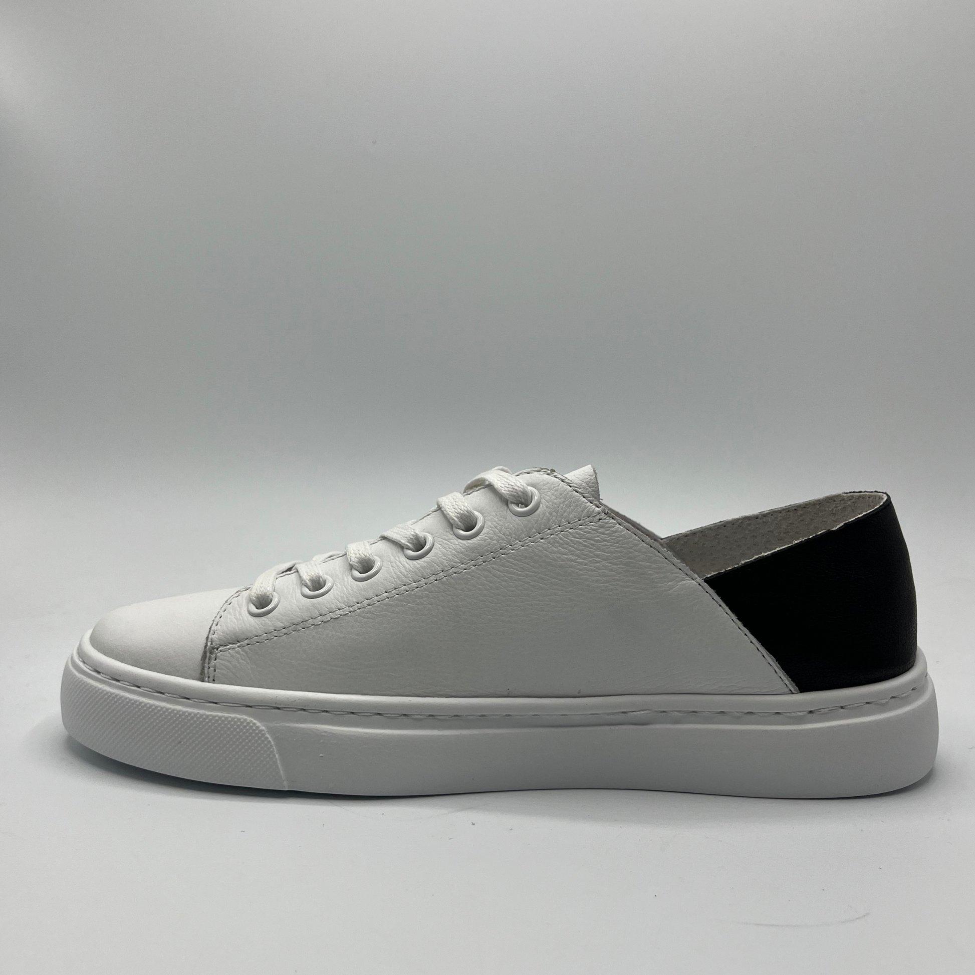 Left facing view of a white leather sneaker with a black heel and white rubber outsole
