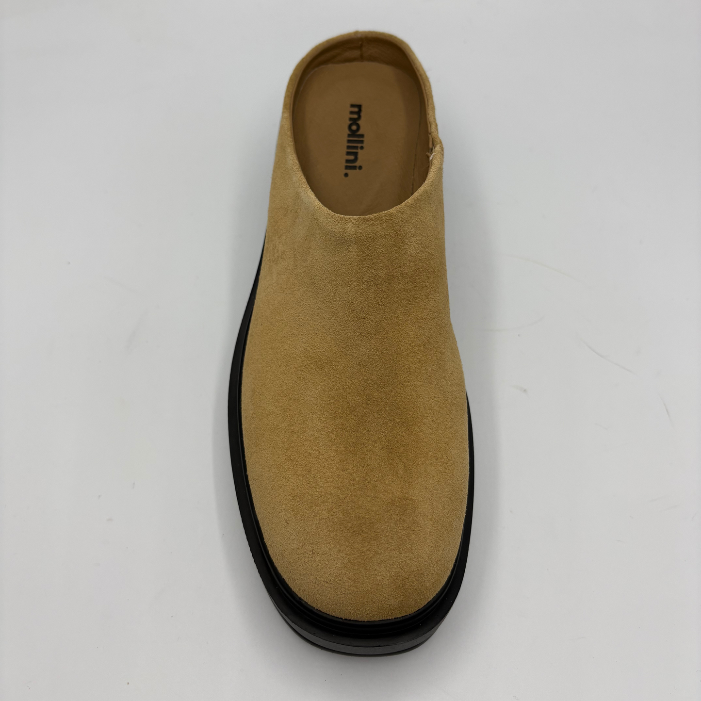 A single tan suede slip-on mule shoe with a black sole, photographed from a top-down perspective on a light gray background. The brand name 'mollini.