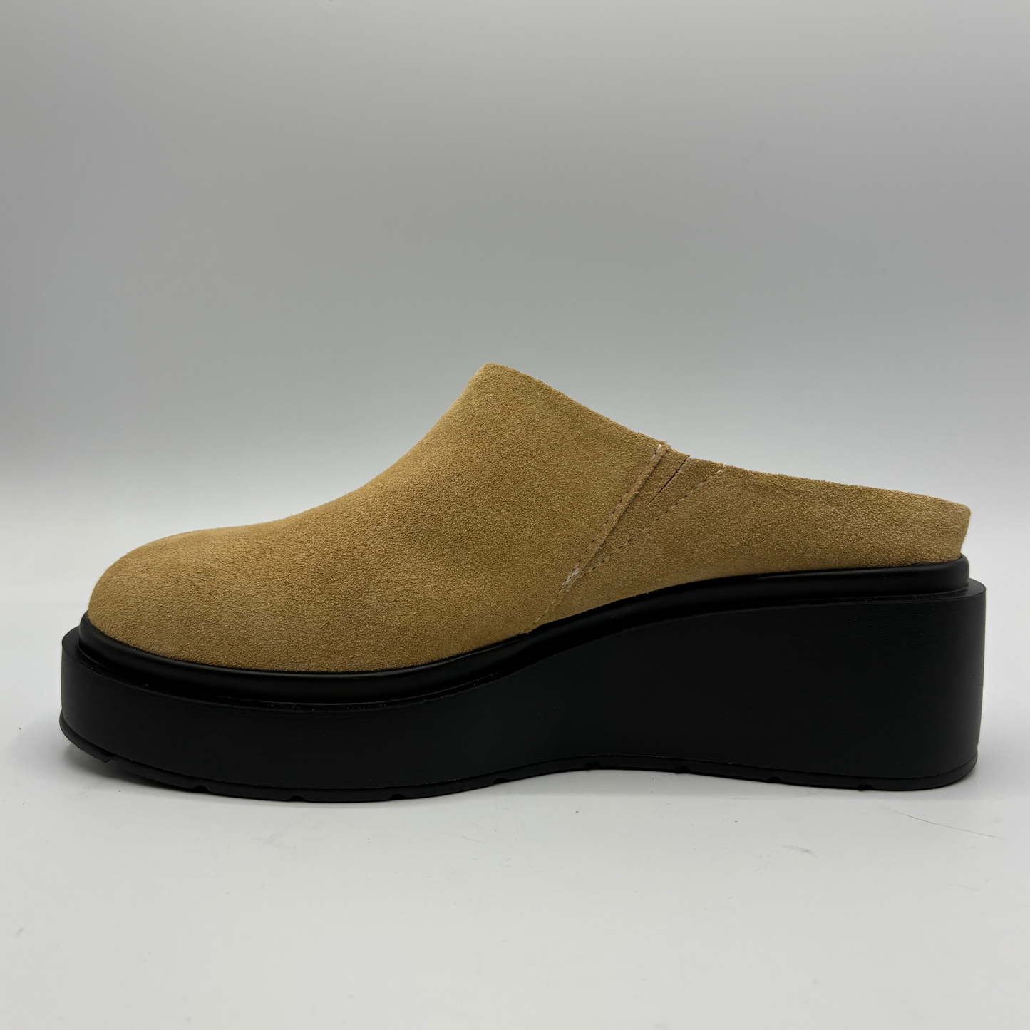 A single platform mule shoe in tan suede with a chunky black wedge sole, shown in a side profile against a neutral gray background.