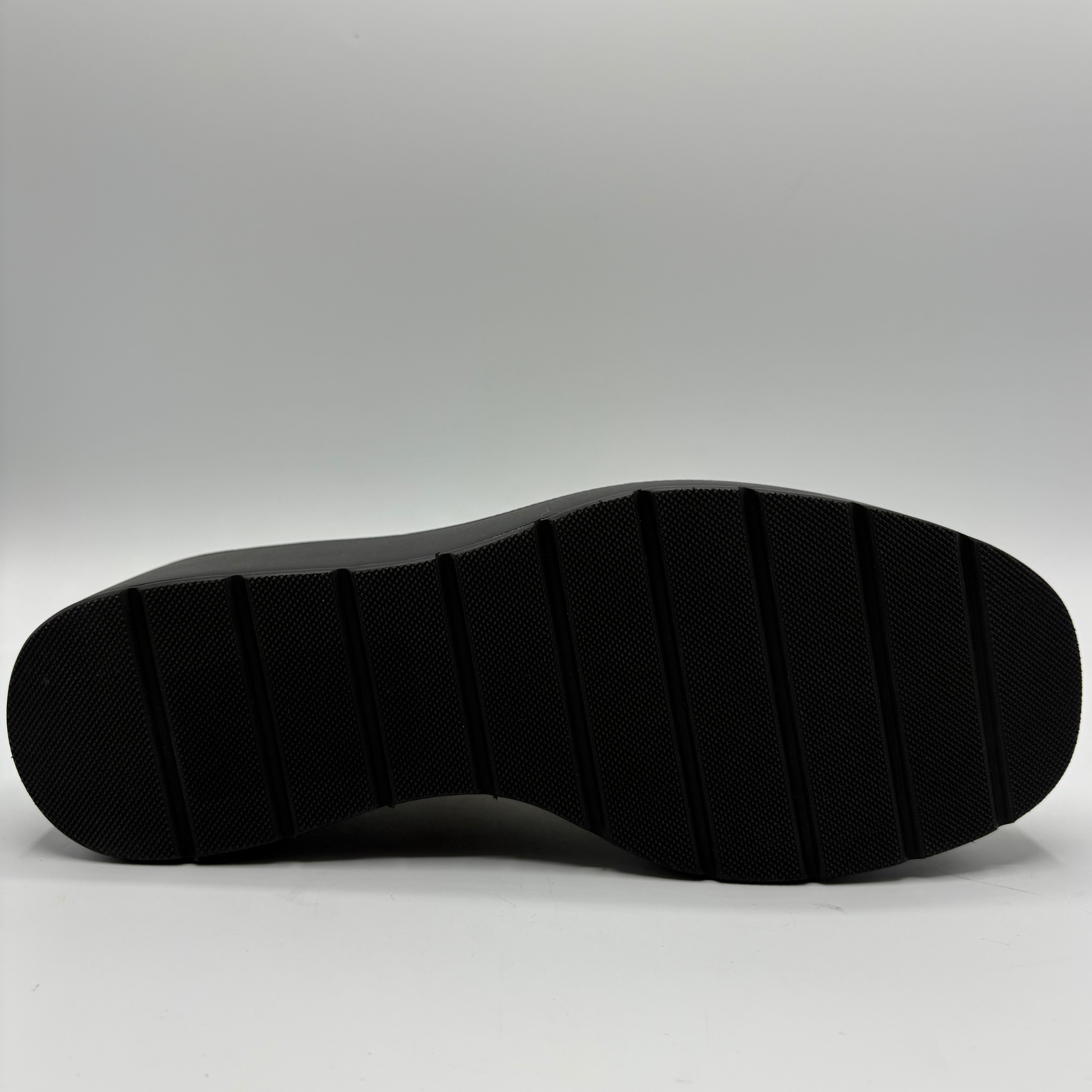 The black textured rubber outsole of a shoe, shown from a top-down view against a light gray studio background.