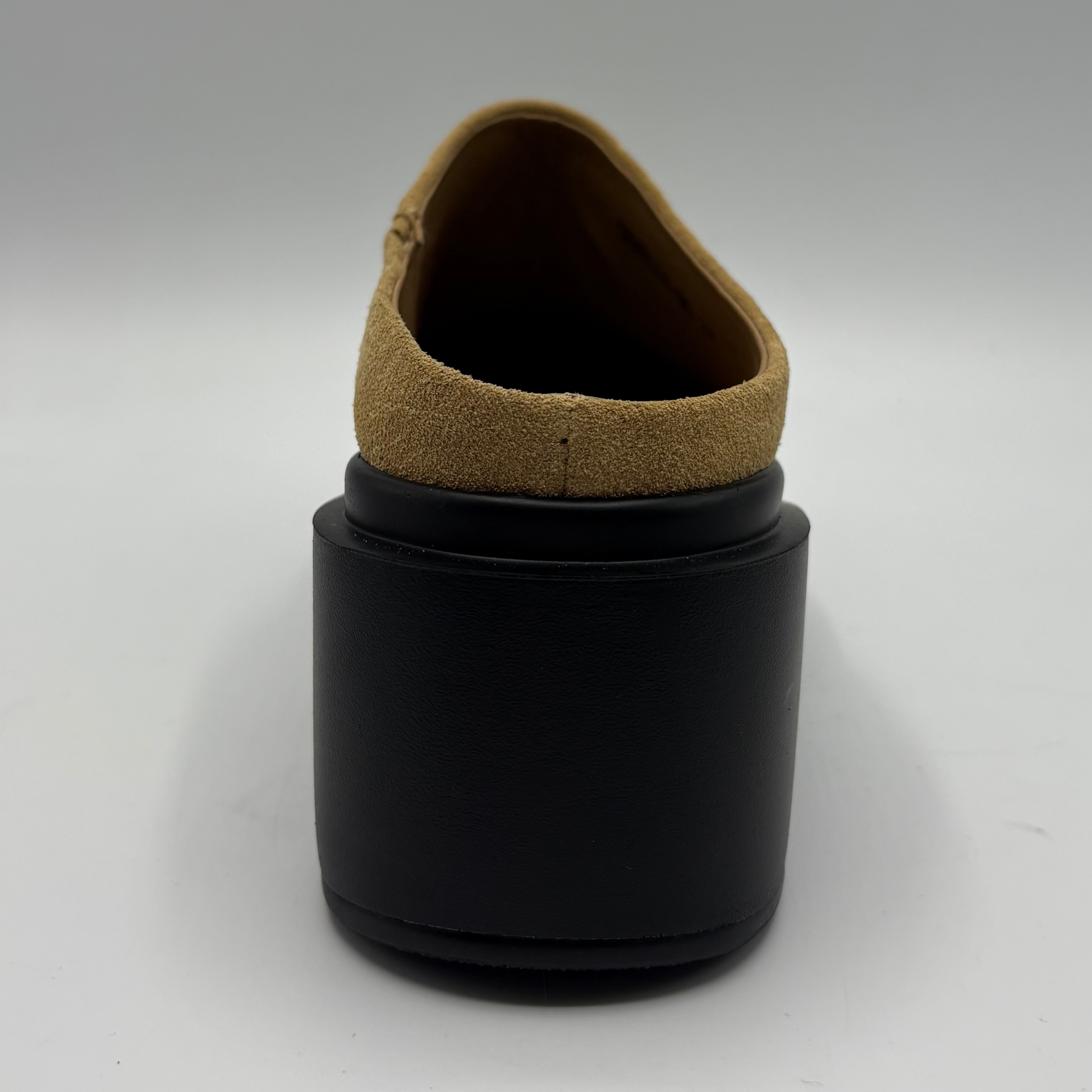 A single shoe shown from the back, featuring a chunky black platform heel and a tan suede or nubuck collar lining, photographed on a neutral light gray background.