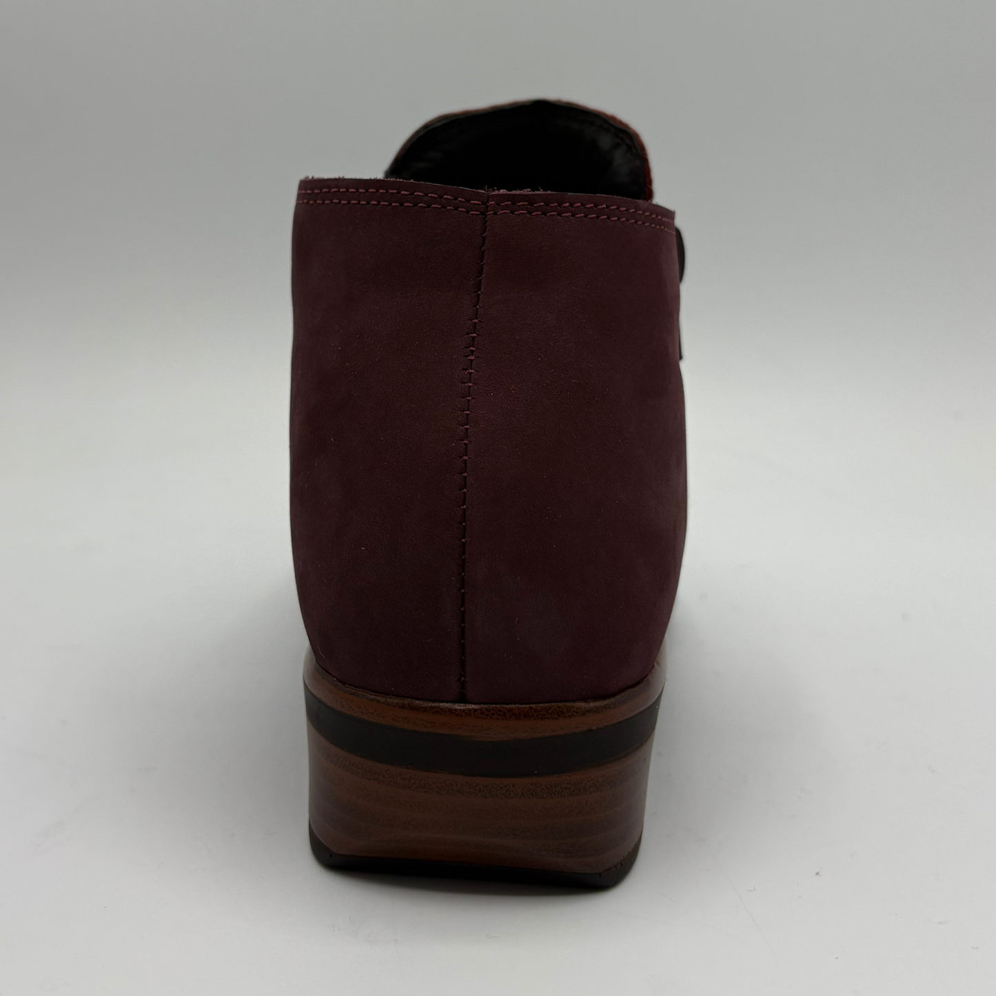 A single burgundy suede ankle boot shown from the back, featuring a stacked wooden-look heel with a black stripe and a black interior lining, set against a neutral gray background.