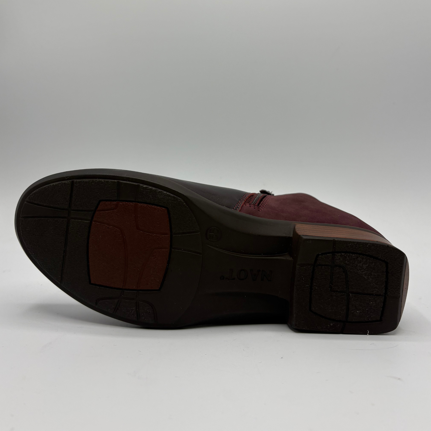 A dark burgundy leather ankle boot with side zipper details, photographed from a top-down angle on a light gray background.