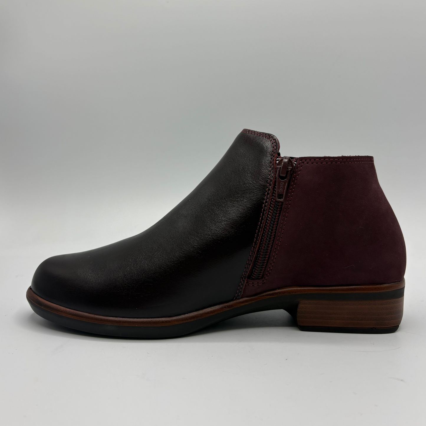 A dark burgundy leather ankle boot with side zipper details, photographed from a top-down angle on a light gray background.