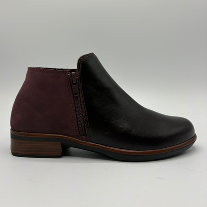 A dark burgundy leather ankle boot with side zipper details, photographed from a top-down angle on a light gray background.
