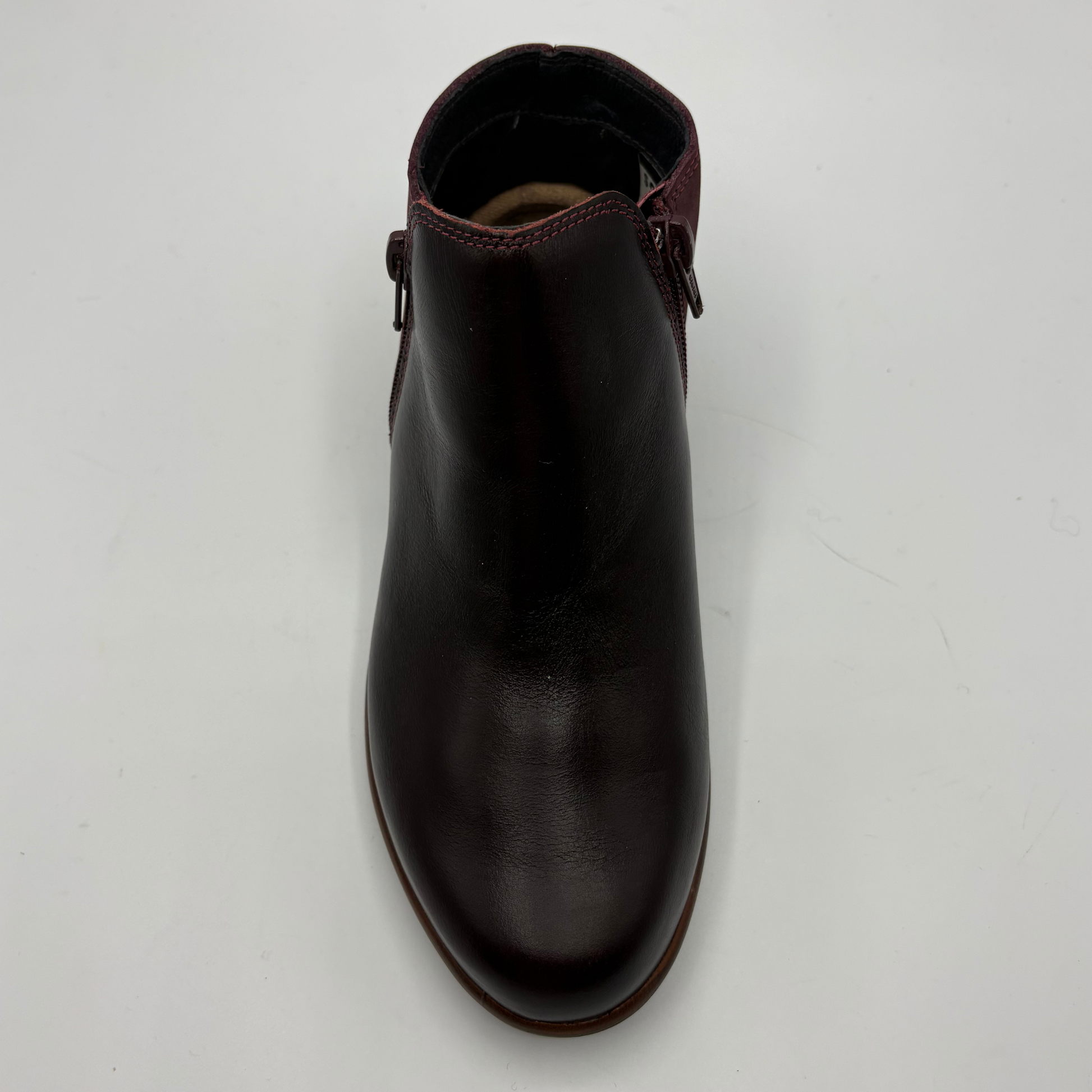 A dark burgundy leather ankle boot with side zipper details, photographed from a top-down angle on a light gray background.