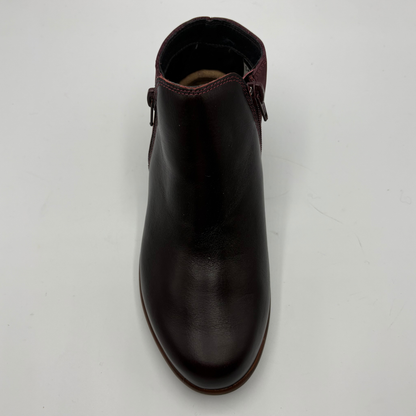 A dark burgundy leather ankle boot with side zipper details, photographed from a top-down angle on a light gray background.