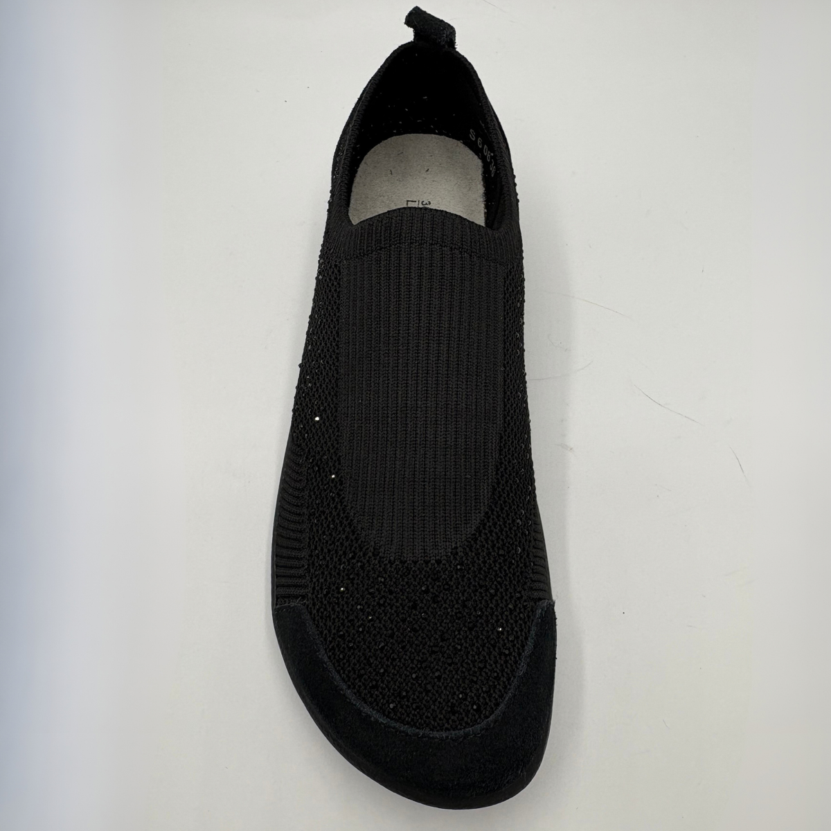 A single black slip-on knit shoe with a textured knit upper and a black sole, photographed from a top-down angle on a light gray background.