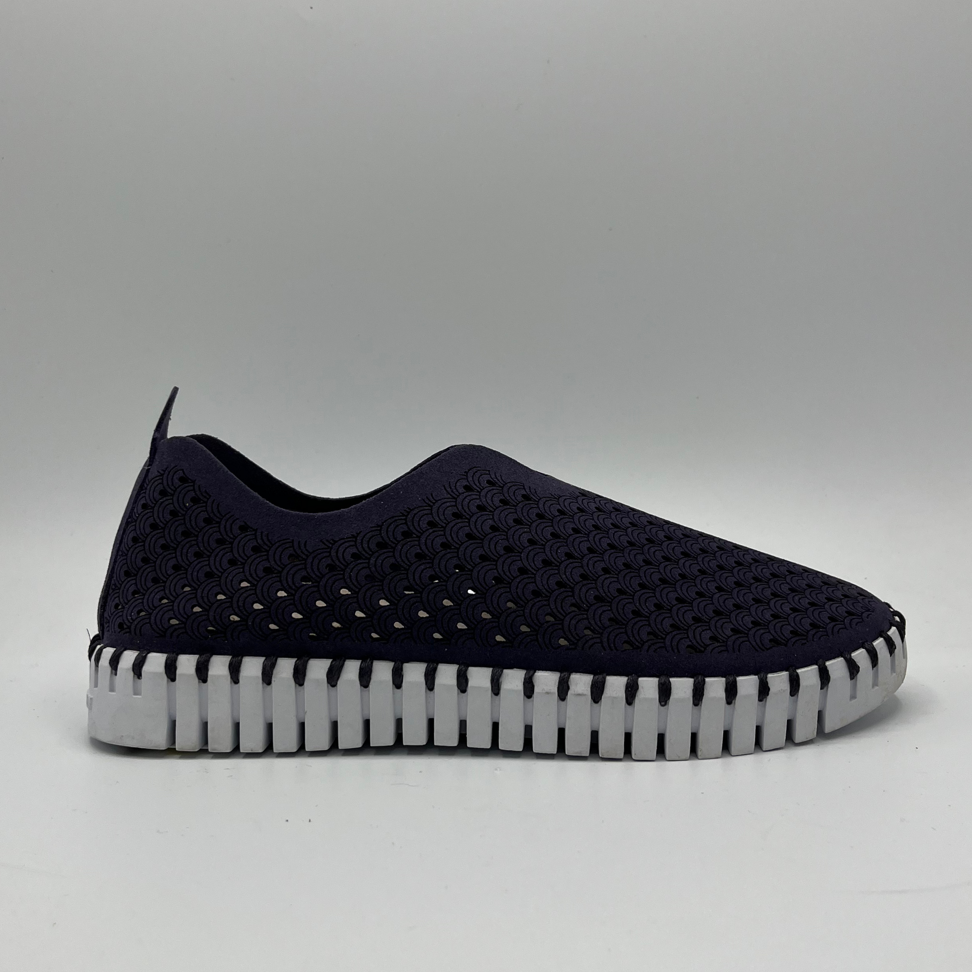 Right facing view of navy coloured slip on shoe with an intricate laser cut upper and white rubber outsole.