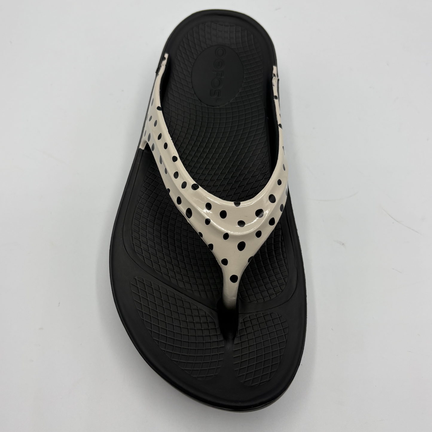 Black sandal with white polka dot strap on a light gray background