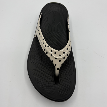 Black sandal with white polka dot strap on a light gray background