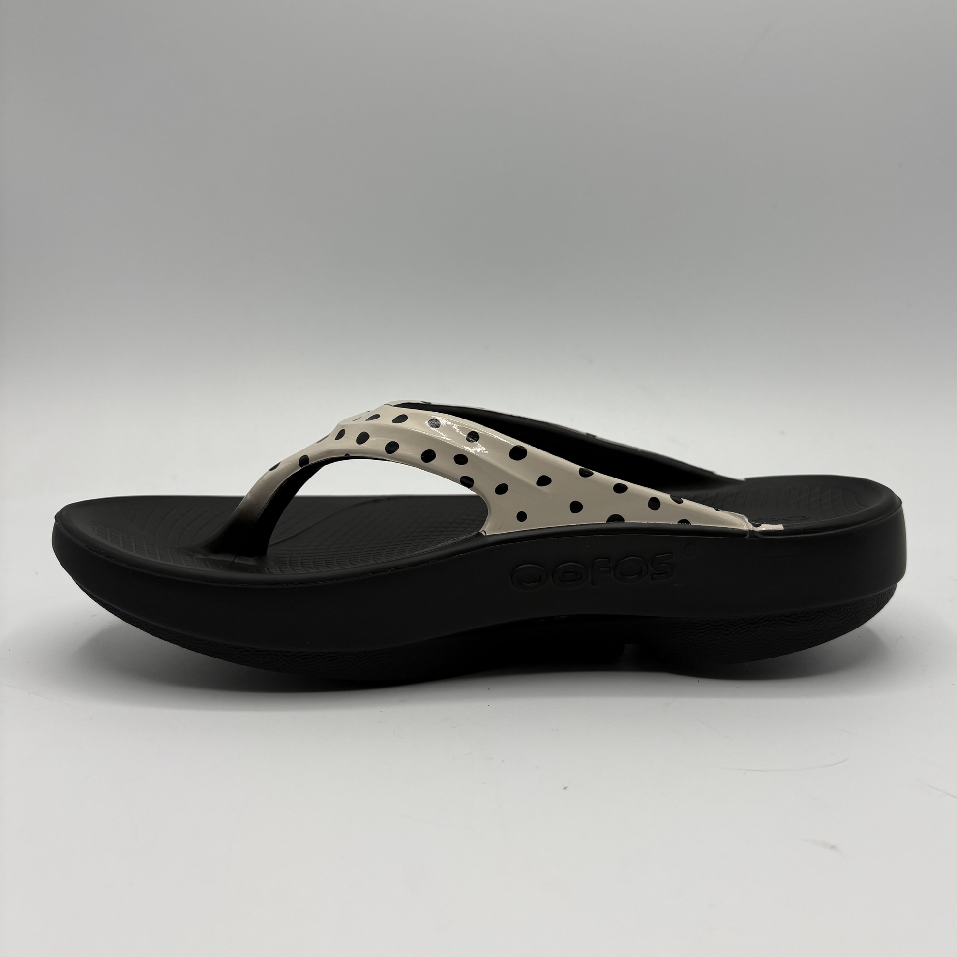 Black sandal with beige polka dot design on a gray background