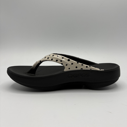 Black sandal with beige polka dot design on a gray background