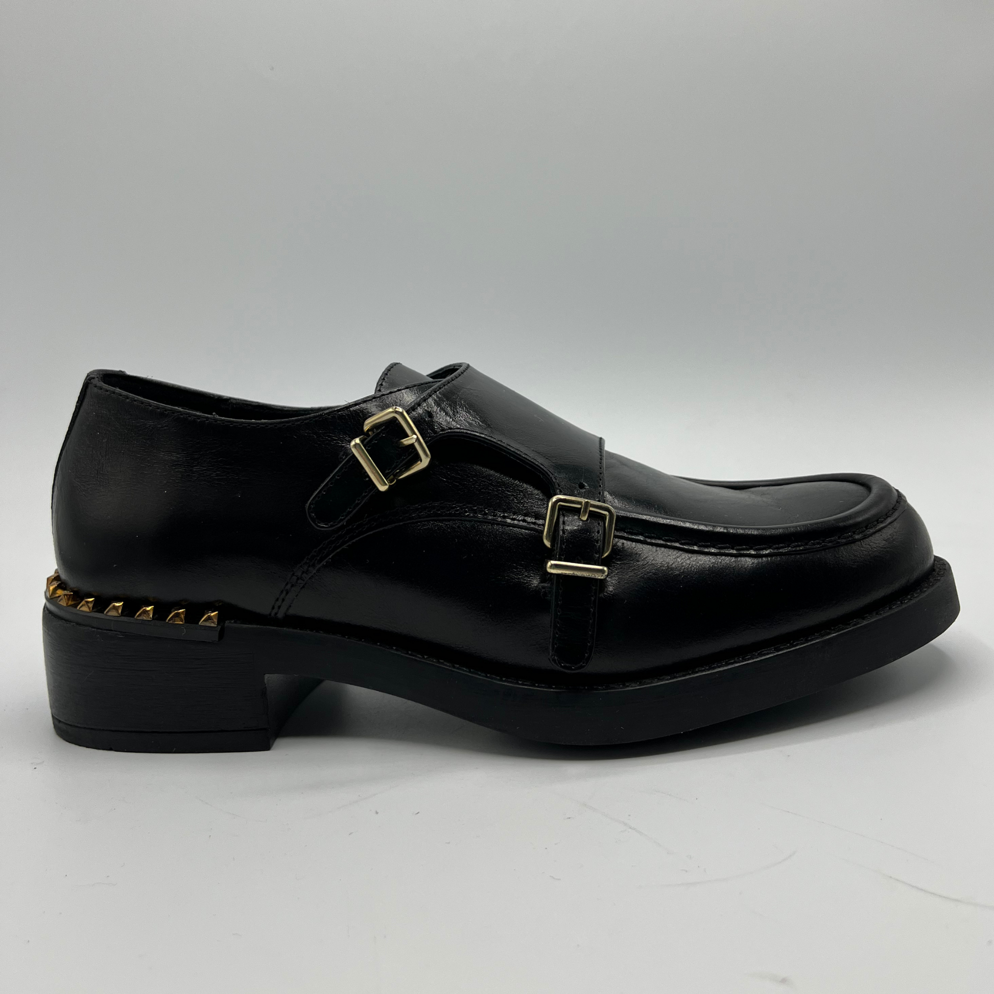 Black leather shoe with gold buckles on a white background
