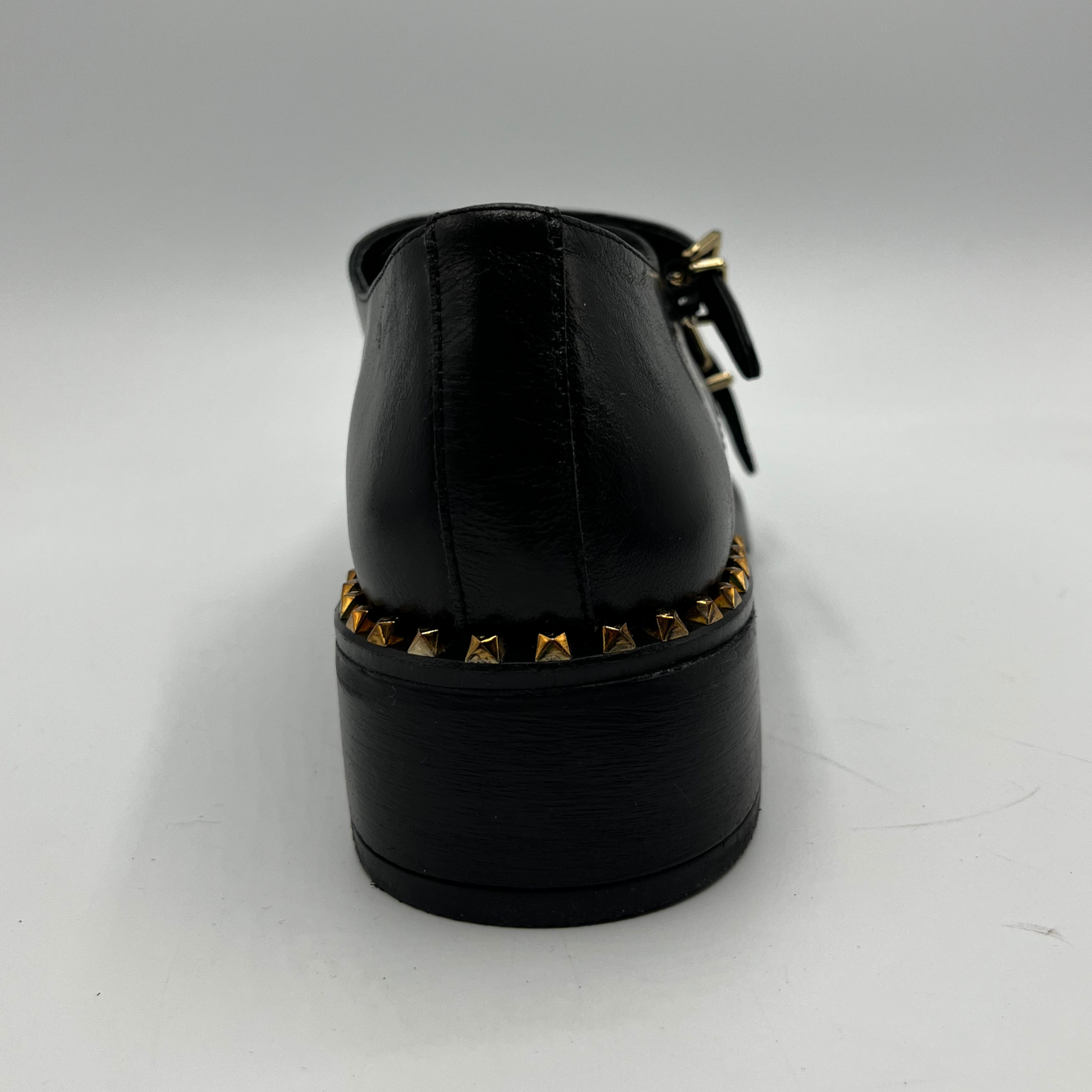 Black shoe with gold studs on a white background