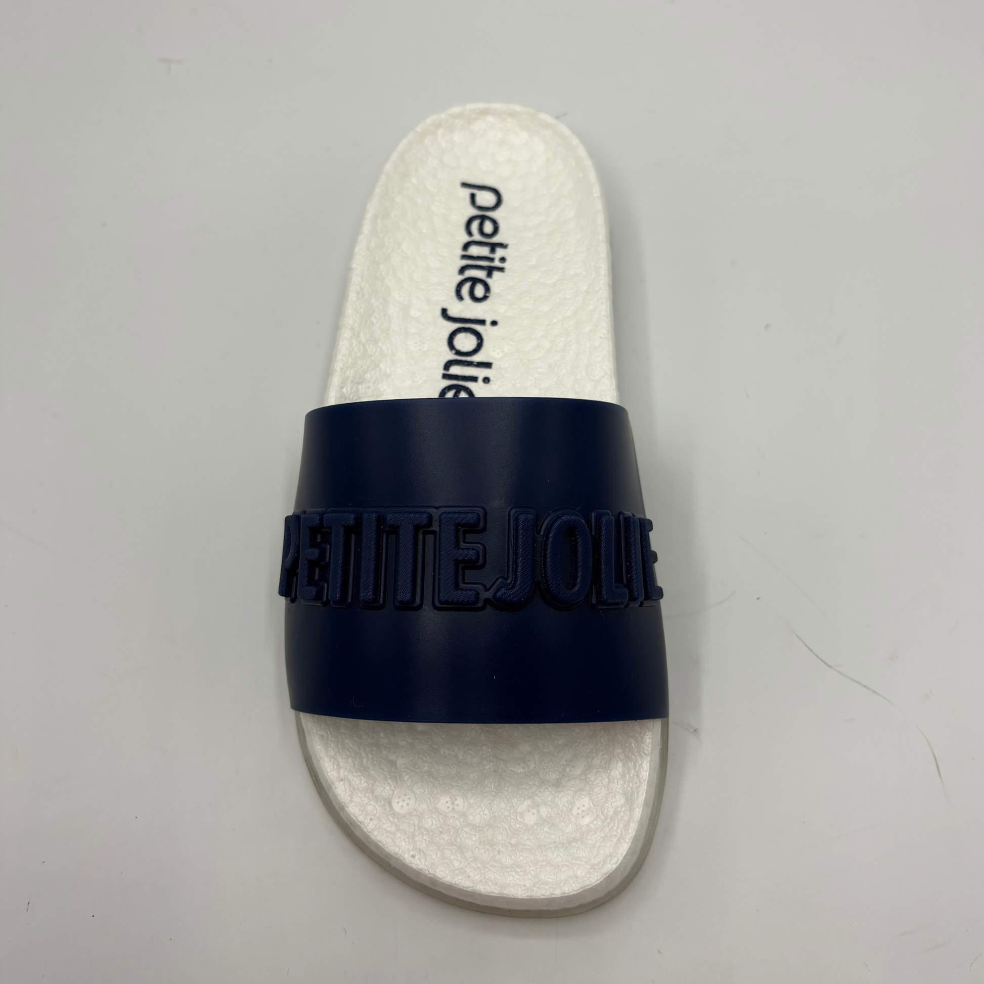 White slide sandal with navy strap on a gray background