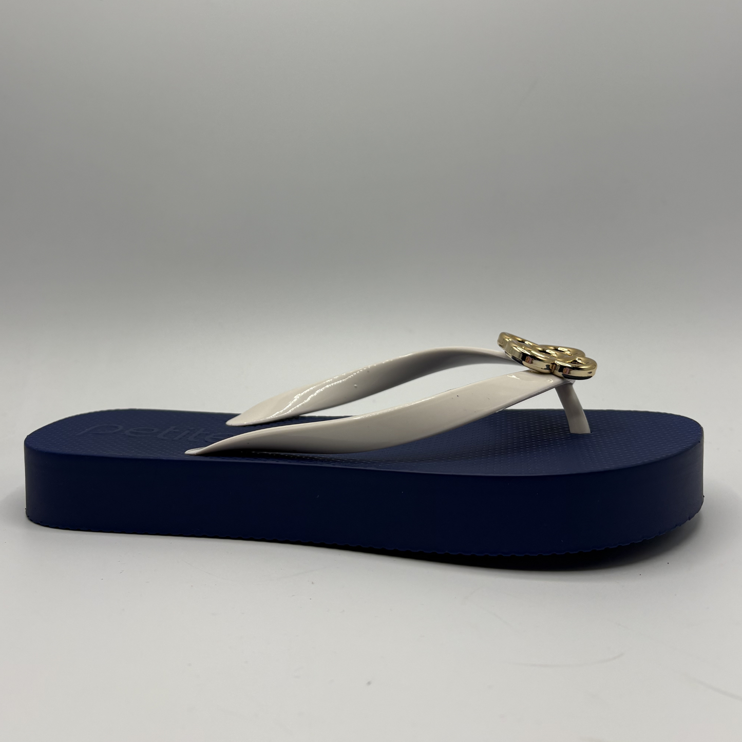 Navy blue and white sandal with a gold embellishment on a gray background
