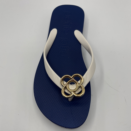 Navy blue sandal with a gold flower buckle on a light gray background