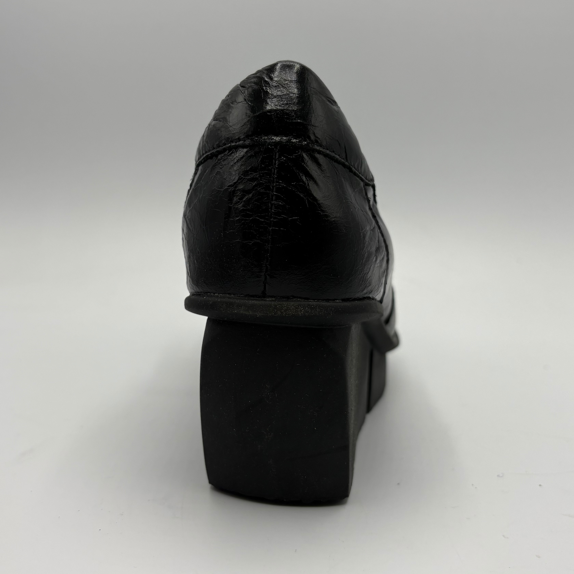 A black leather platform shoe shown from a rear three-quarter angle, highlighting the textured leather upper and chunky platform heel, set against a plain light gray background.