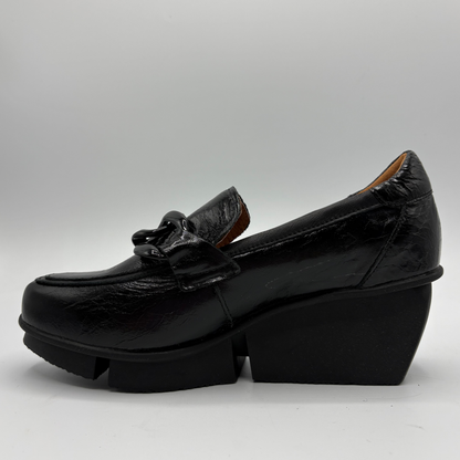 A single black leather platform loafer with a chunky block heel and a decorative bow detail on the vamp, photographed against a neutral gray studio background.
