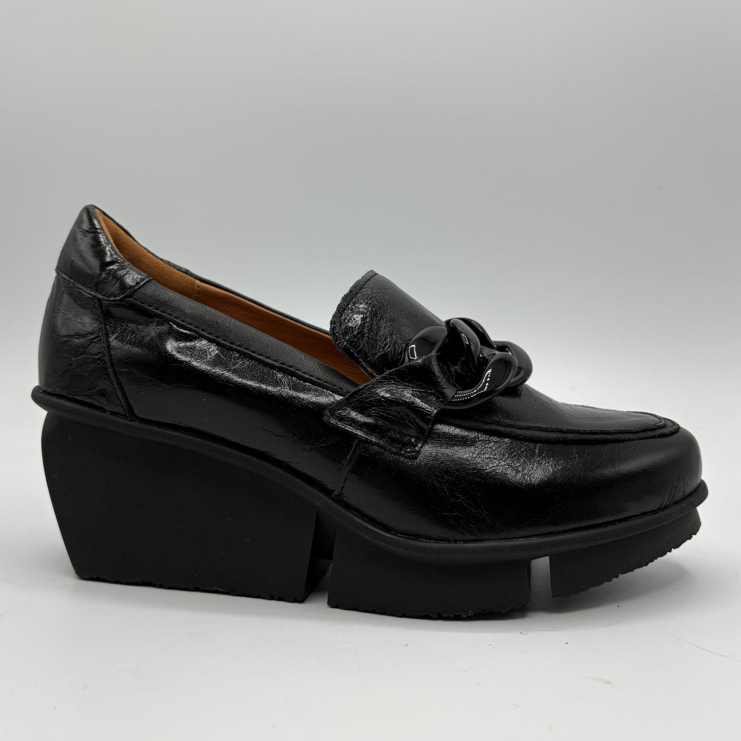 A single black leather loafer-style shoe with a chunky platform wedge and a decorative bow detail on the vamp, photographed on a light gray studio background.