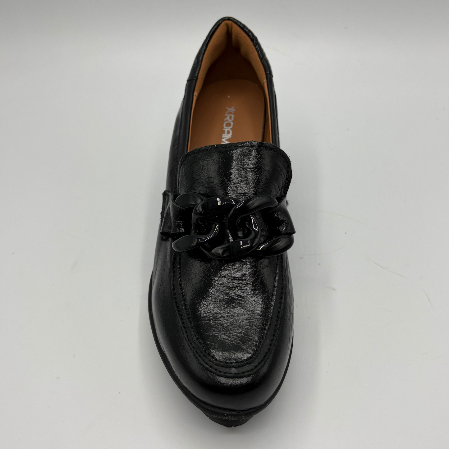 A single black leather loafer with a chunky black chain detail across the vamp, photographed from a top-down angle on a light gray background.