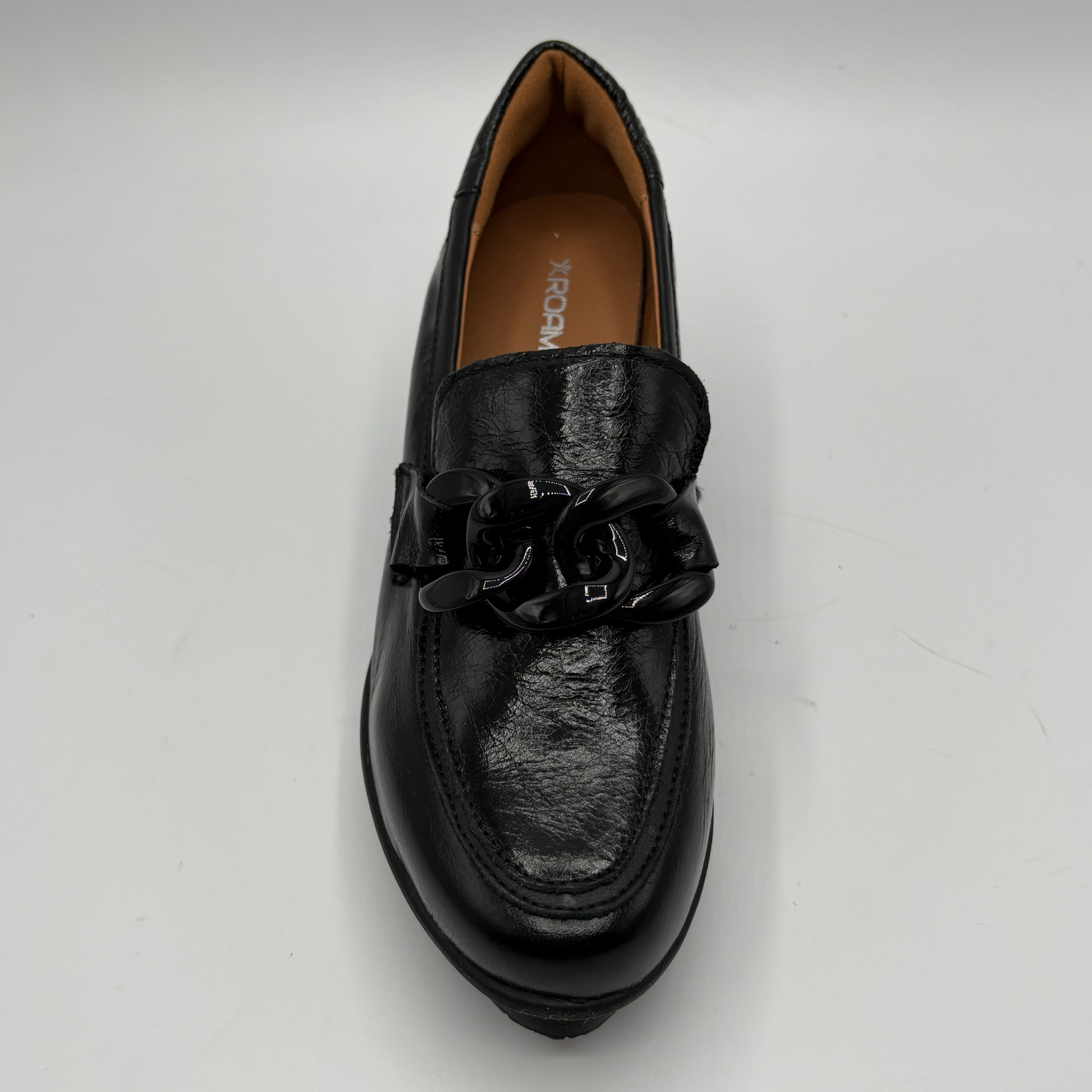A single black leather loafer with a chunky black chain detail across the vamp, photographed from a top-down angle on a light gray background.