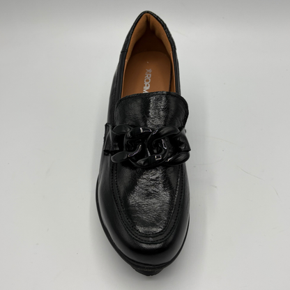 A single black leather loafer with a chunky black chain detail across the vamp, photographed from a top-down angle on a light gray background.