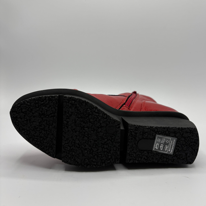 A close-up shot of the sole of a red leather boot, showing the textured black rubber outsole and a small label on the heel, set against a plain light gray background.