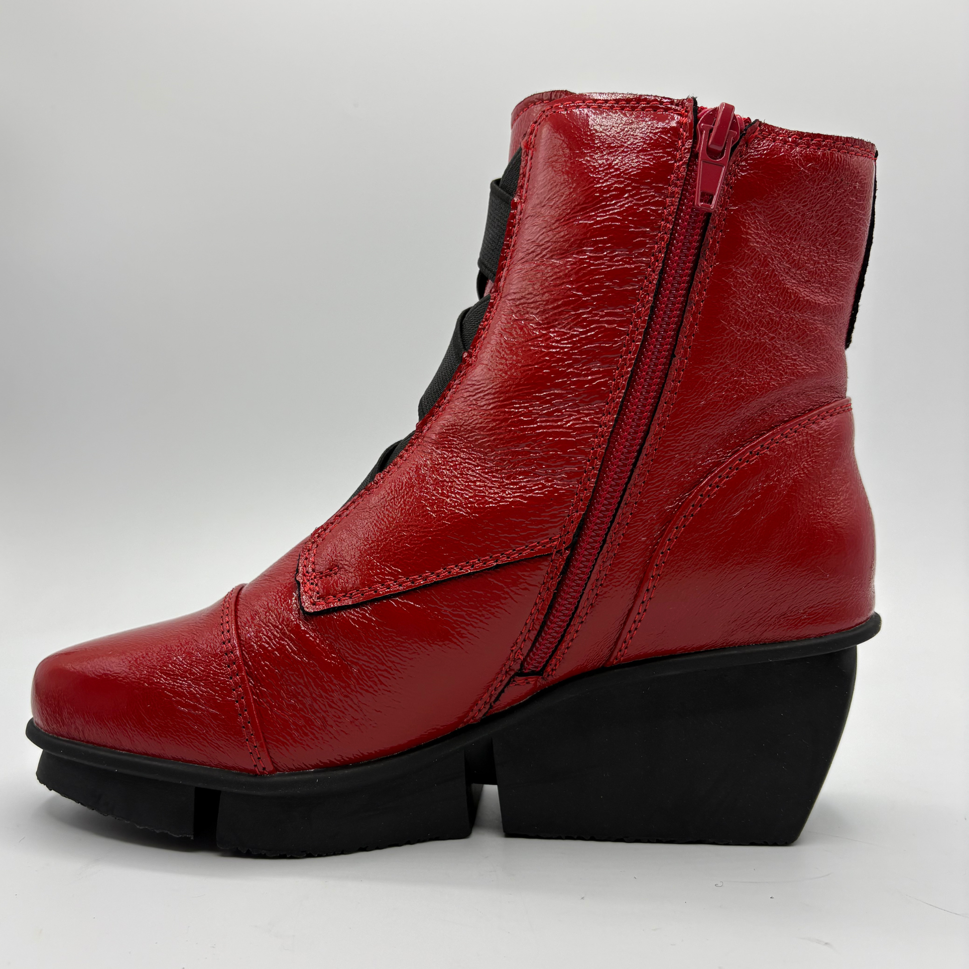 A red leather ankle boot with a black wedge heel and black side zipper, shown from a side profile view against a light gray background.