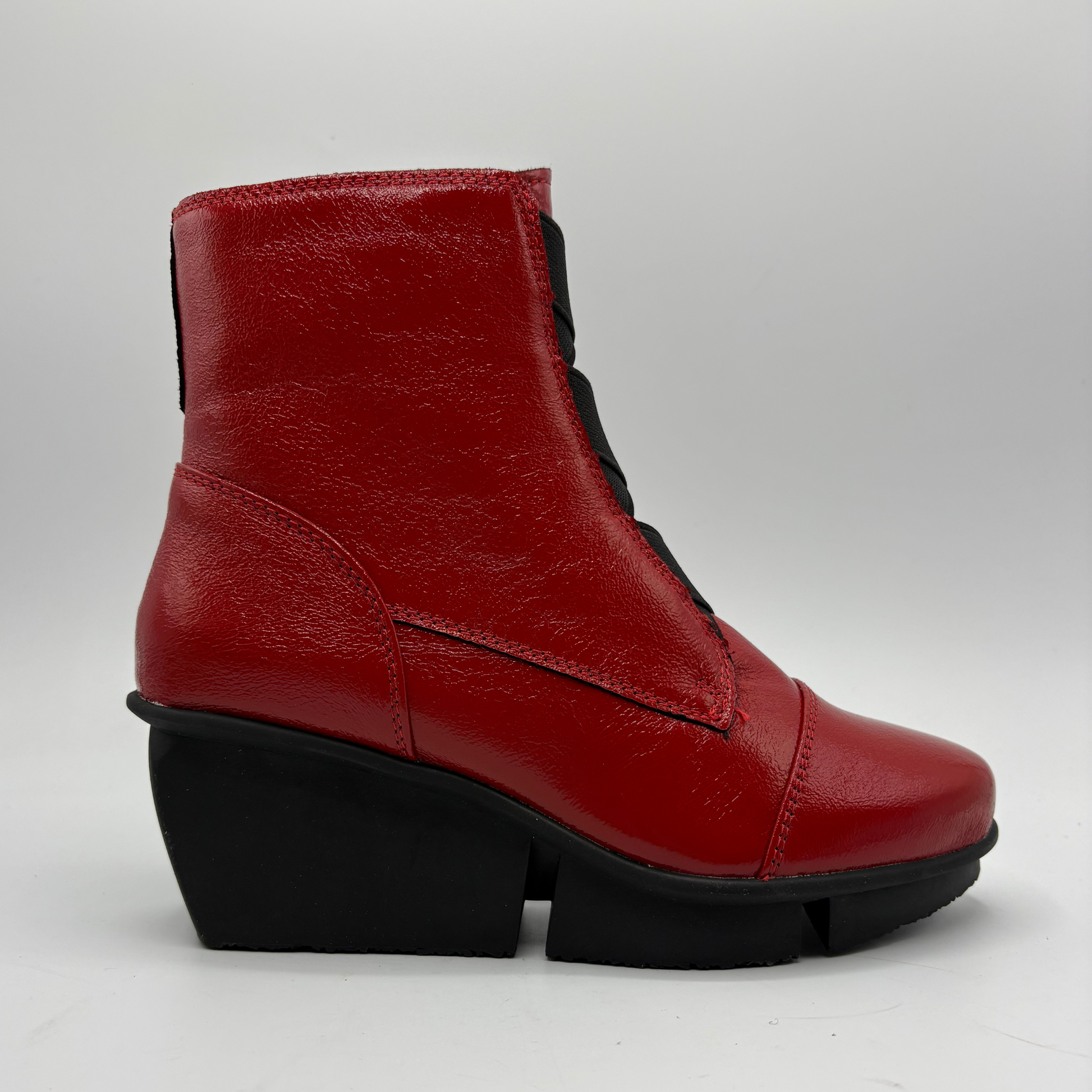 A red leather ankle boot with a chunky black wedge heel and black laces, shown from a side profile on a light gray background.