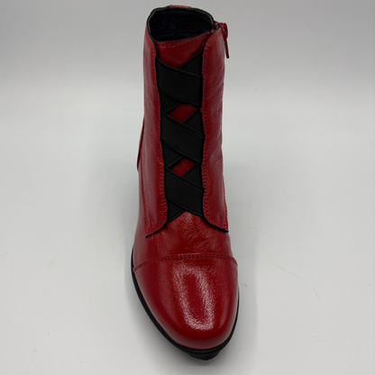 A red leather ankle boot with black elastic criss-cross straps down the front, shown from a front-facing angle on a light gray background.