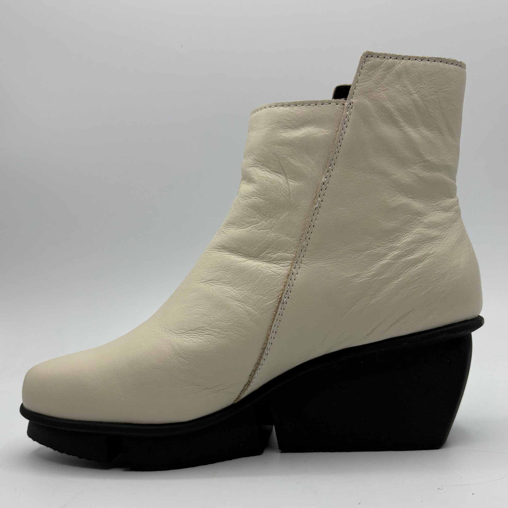 A single women's ankle boot in off-white leather with a chunky black wedge heel and sole, shown from a side profile view against a light gray background.