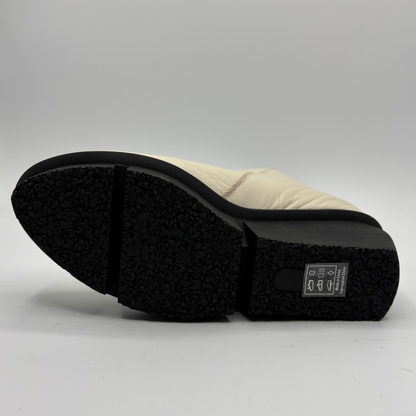 A close-up shot of the sole of a light beige boot, showing a black textured rubber outsole and a small black brand label on the heel.