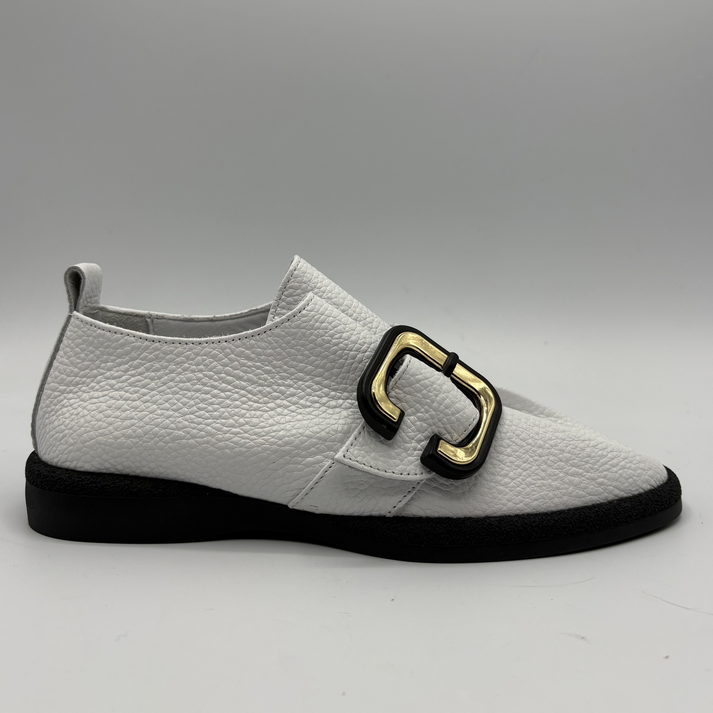 Right facing view of a white leather shoe with a gold buckle