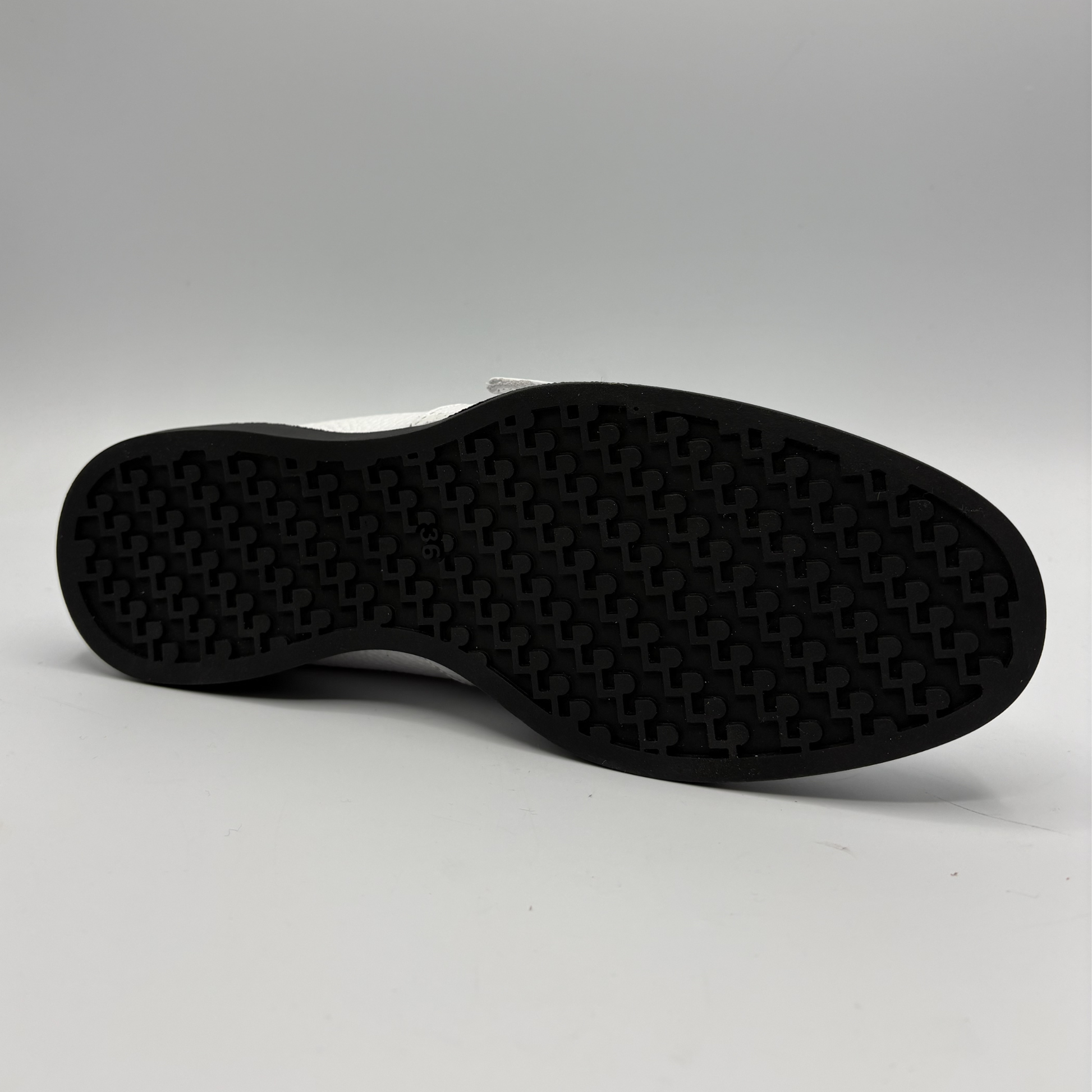 Bottom view of a white leather shoe with a gold buckle