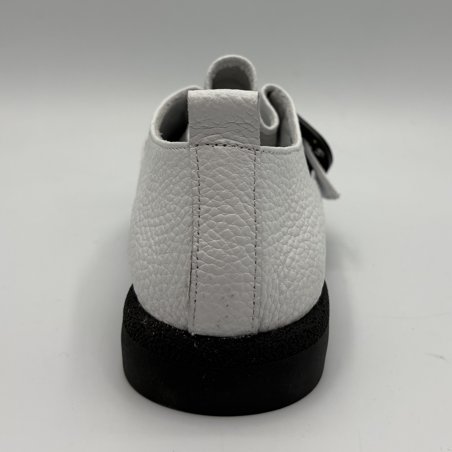 Back view of a white leather shoe with a gold buckle