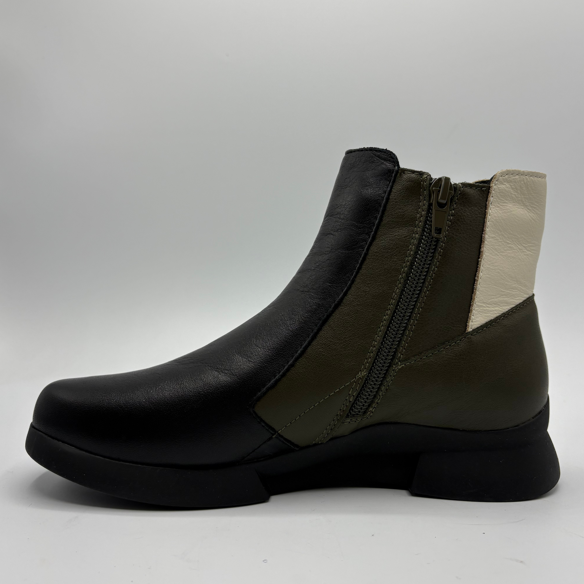 A women's ankle boot in black leather with olive green side panels and a cream-colored inner heel detail, featuring a side zipper, shown against a neutral gray background.
