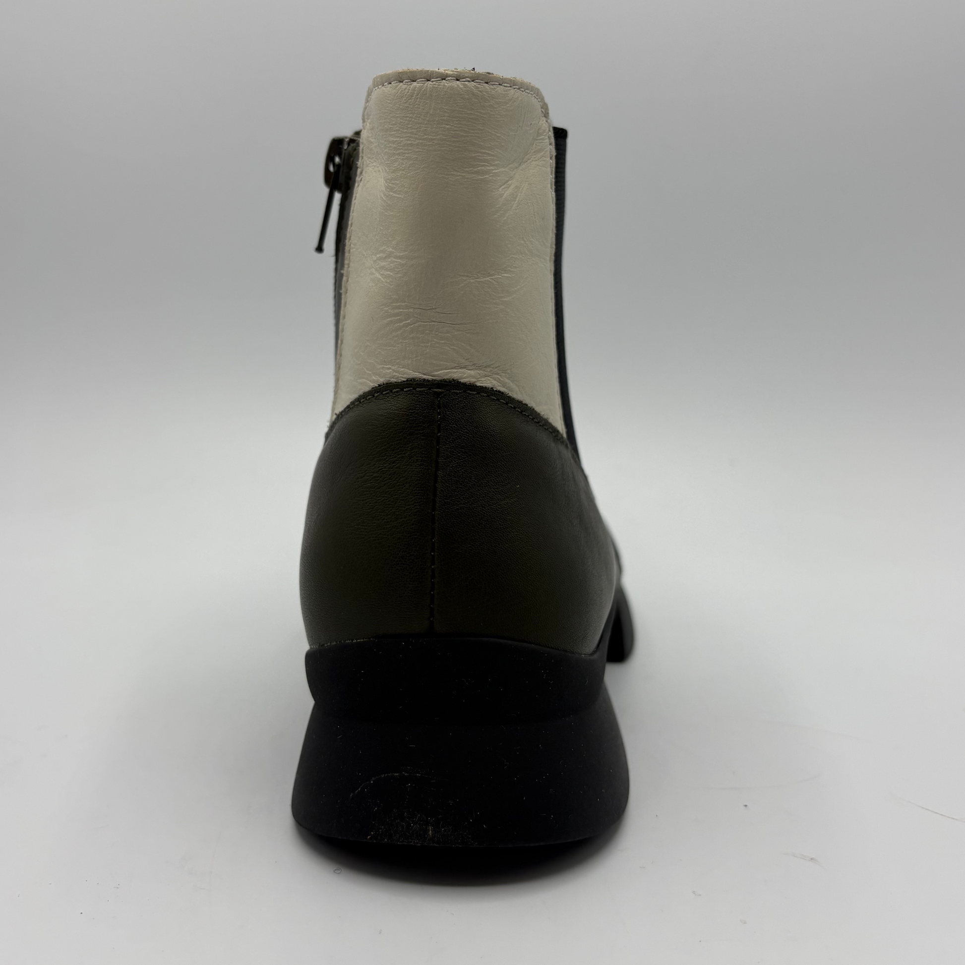 A single black leather ankle boot shown from the back on a light gray studio background, featuring a cream-colored leather back panel and a side zipper.
