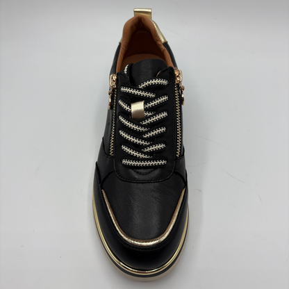 A black leather side-zip sneaker with decorative white and gold braided laces, gold-tone hardware, and a gold trim accent along the toe and sole, shown from a top-down view on a light gray background.