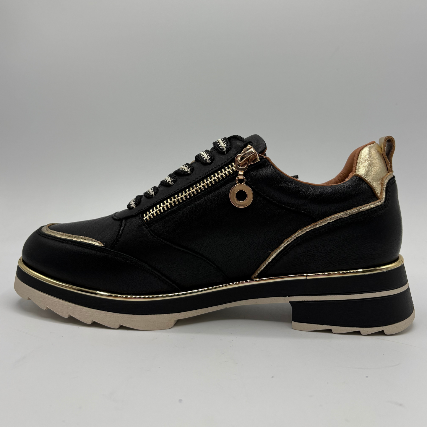 A black leather low-top sneaker with a chunky platform sole, featuring a gold-tone side zipper, decorative gold piping, and a gold pull tab on the heel.