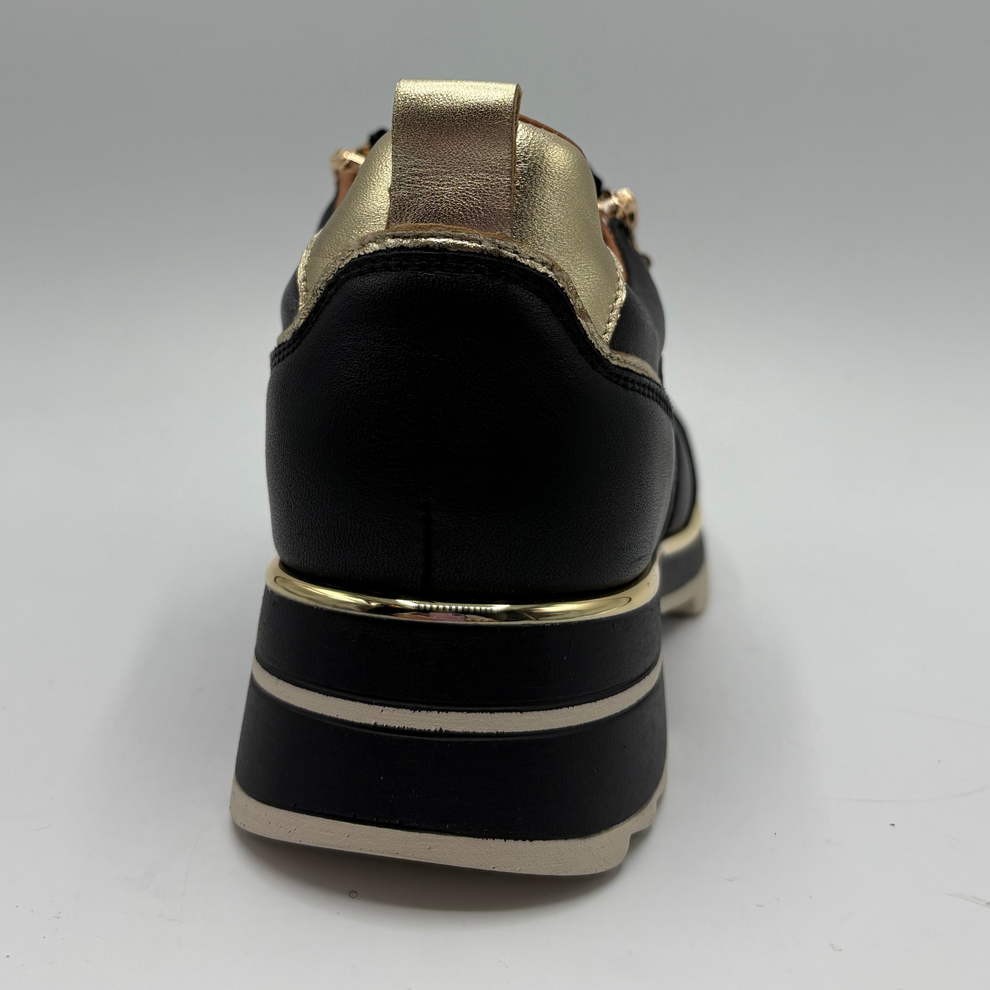 A black leather platform shoe with metallic gold accents on the heel tab, eyelets, and sole, photographed from a rear three-quarter angle against a neutral gray background.