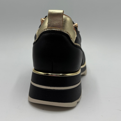 A black leather platform shoe with metallic gold accents on the heel tab, eyelets, and sole, photographed from a rear three-quarter angle against a neutral gray background.