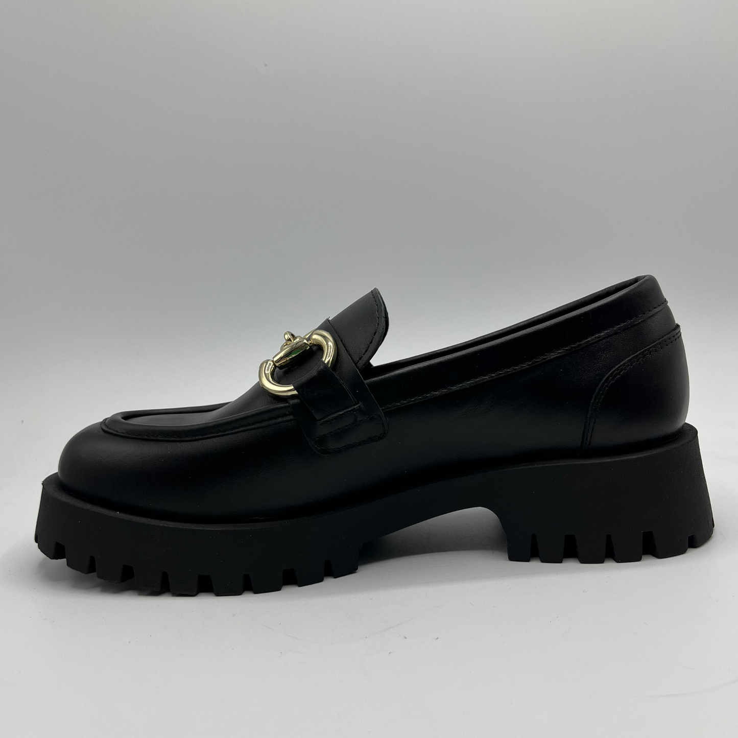 Black loafer shoe with gold buckle on a light gray background