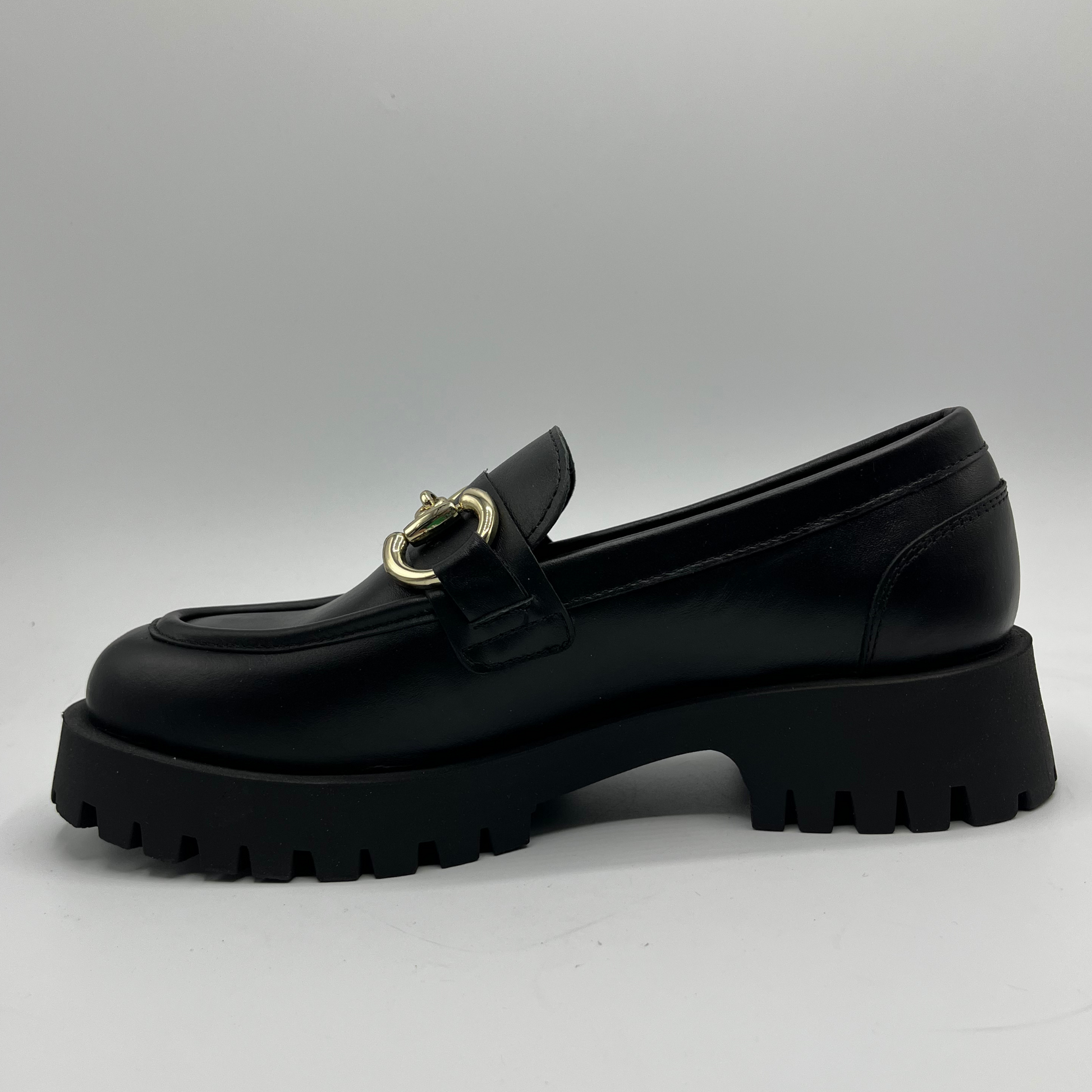 Black loafer shoe with gold buckle on a light gray background