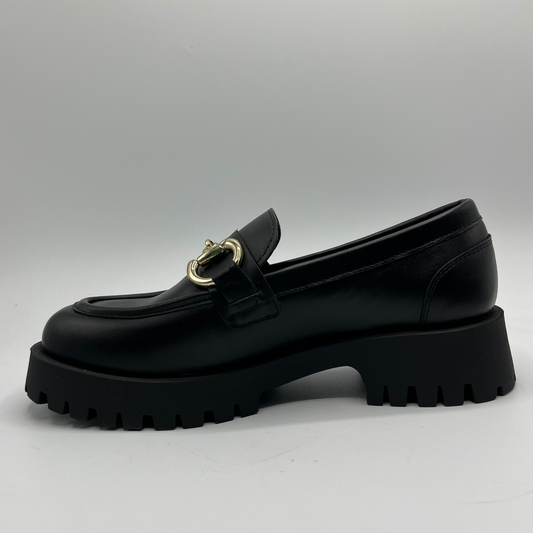 Black loafer shoe with gold buckle on a light gray background