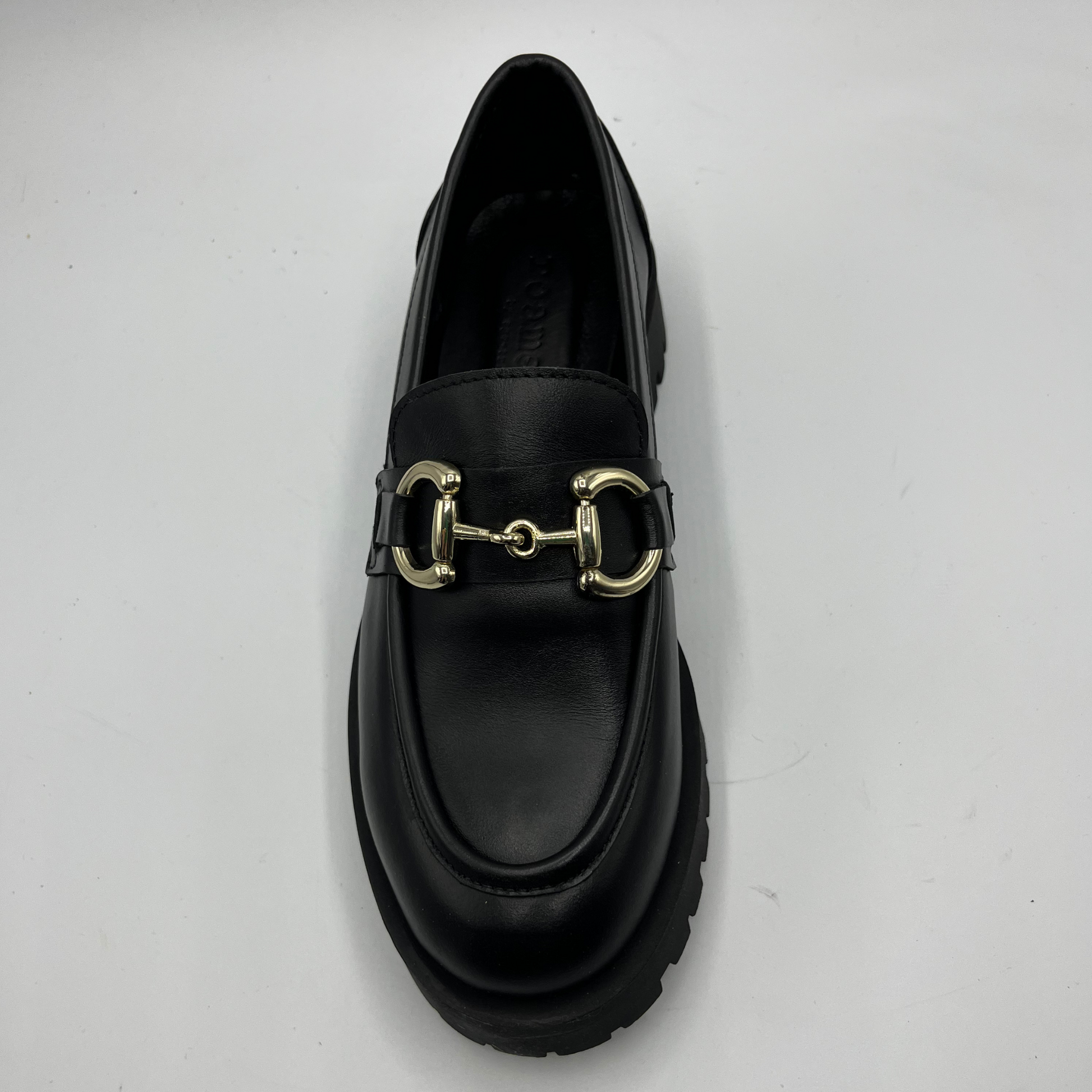 Black loafer with gold buckle on a light gray background