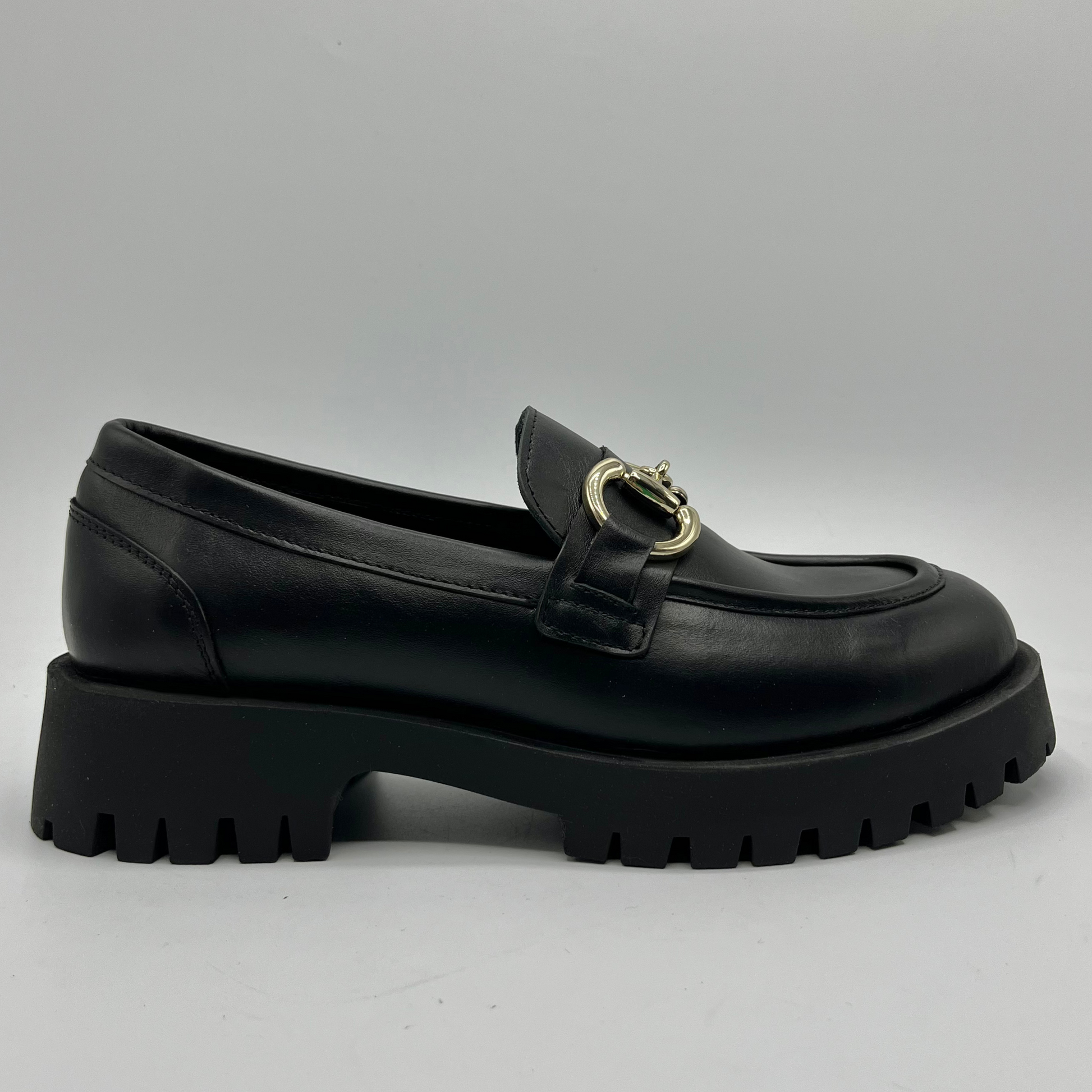 Black loafer shoe with a gold buckle on a gray background