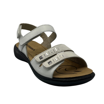 45 degree angled view of white leather sandal with silver details on double toe straps and black rubber outsole